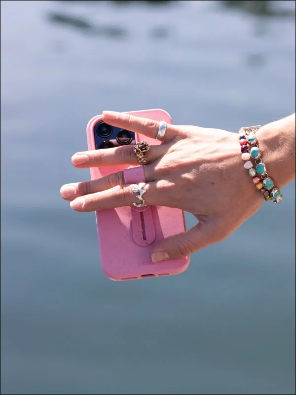 A hand holding a pink Pela phone case with a grip over blue water