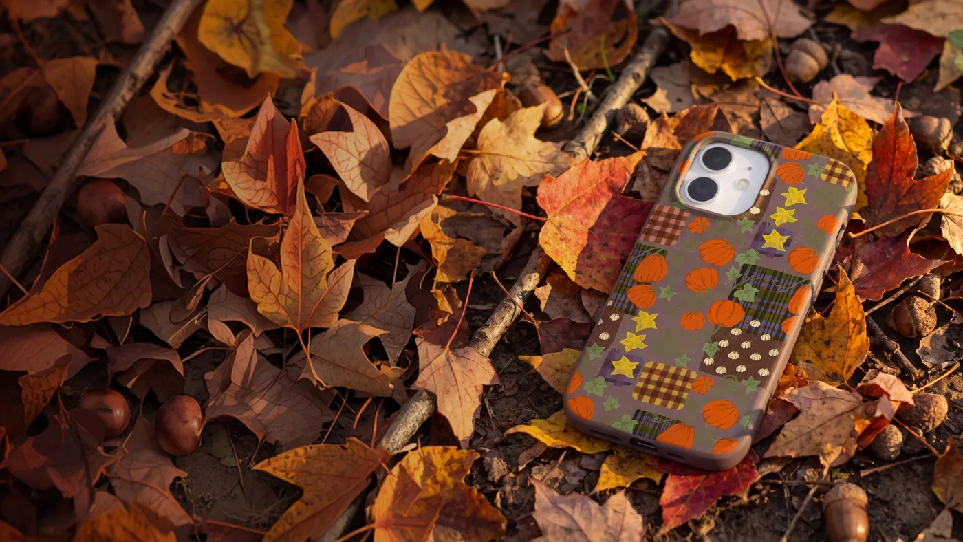 A Pela phone case with an autumn leaf design lying among fallen autumn leaves