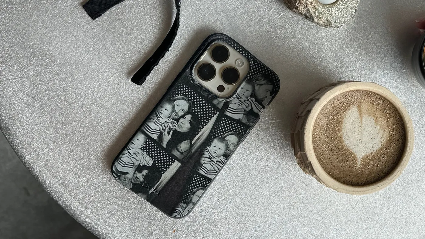 A black Pela phone case with a floral design on a stone table beside a latte