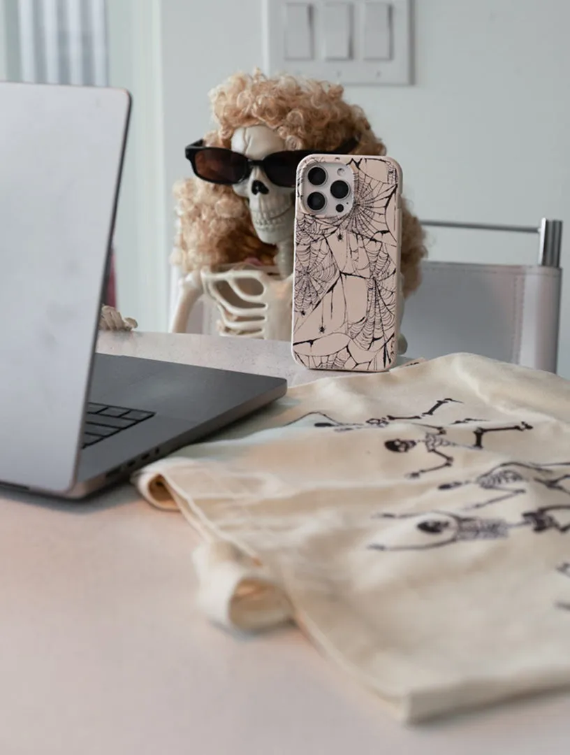 A Pela phone case in front of a laptop beside a tote bag