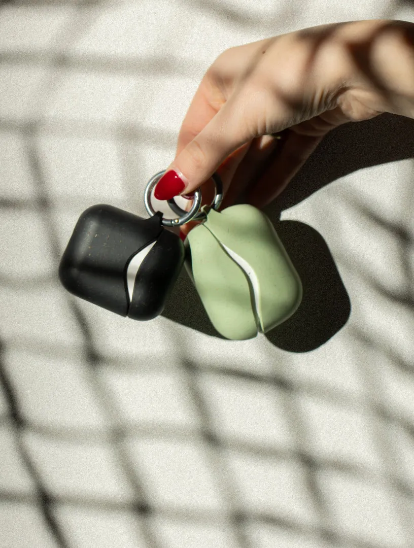 A hand holding two Pela AirPod cases in the shade of a window